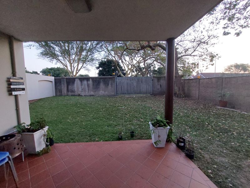 A covered patio area with tiled flooring overlooking a private backyard enclosed by boundary walls and a metal gate.