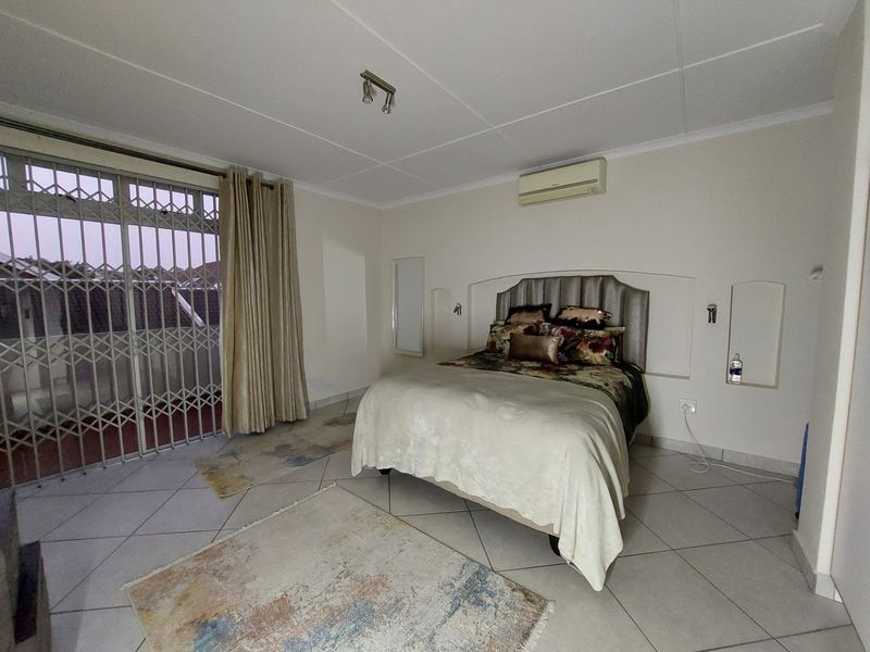 Spacious bedroom featuring tiled flooring, a wall-mounted air conditioner, and a sliding glass door with a security gate leading to an outdoor area.