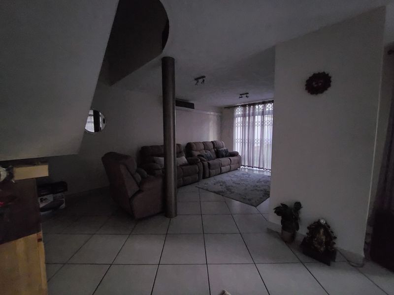 A living room area featuring ceramic floor tiles, a structural support column, and access to a balcony through a security gate.