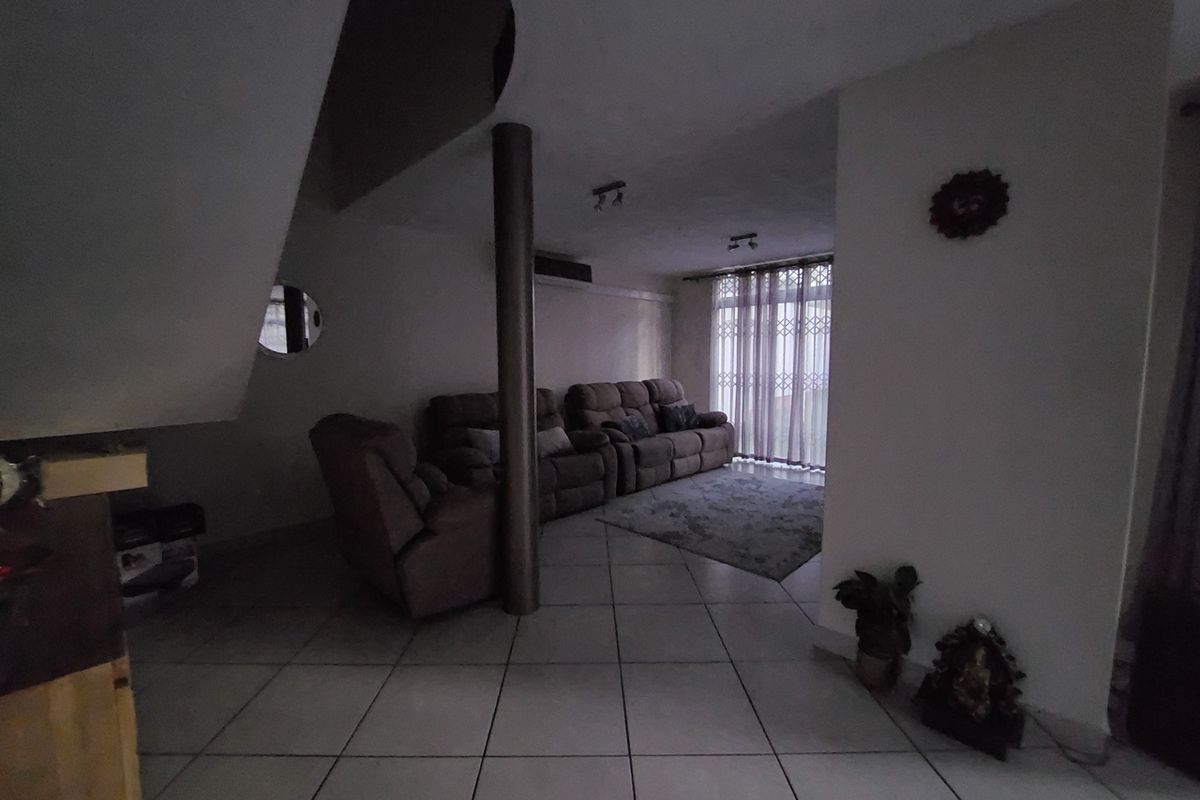 A living room area featuring ceramic floor tiles, a structural support column, and access to a balcony through a security gate.