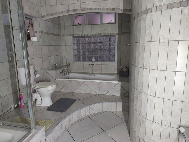 A tiled bathroom featuring a built-in bathtub, a glass block window, a separate shower enclosure, and a toilet.