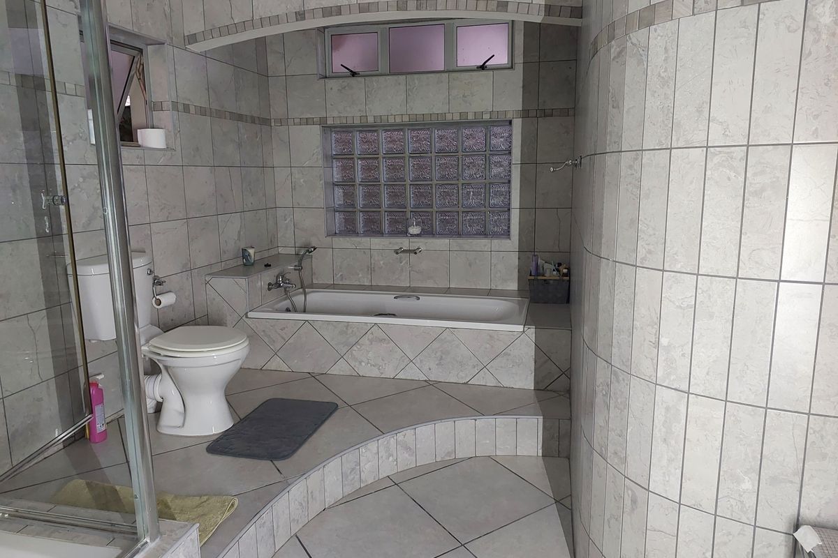 A tiled bathroom featuring a built-in bathtub, a glass block window, a separate shower enclosure, and a toilet.