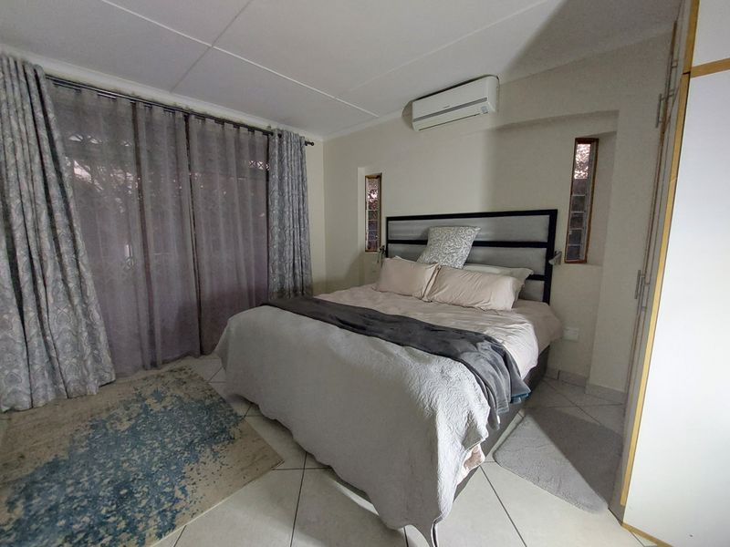 A functional bedroom featuring tiled flooring, built-in cupboards, a wall-mounted air conditioning unit, and natural light through vertical accent windows.