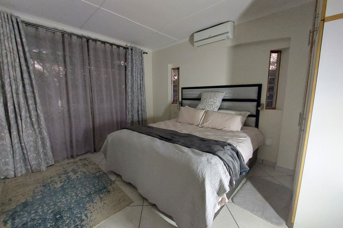 A functional bedroom featuring tiled flooring, built-in cupboards, a wall-mounted air conditioning unit, and natural light through vertical accent windows.