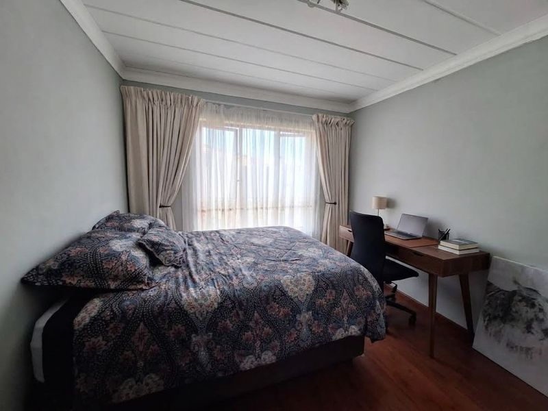 A well-lit bedroom featuring laminate flooring and a neutral color palette, offering a comfortable and functional living space.