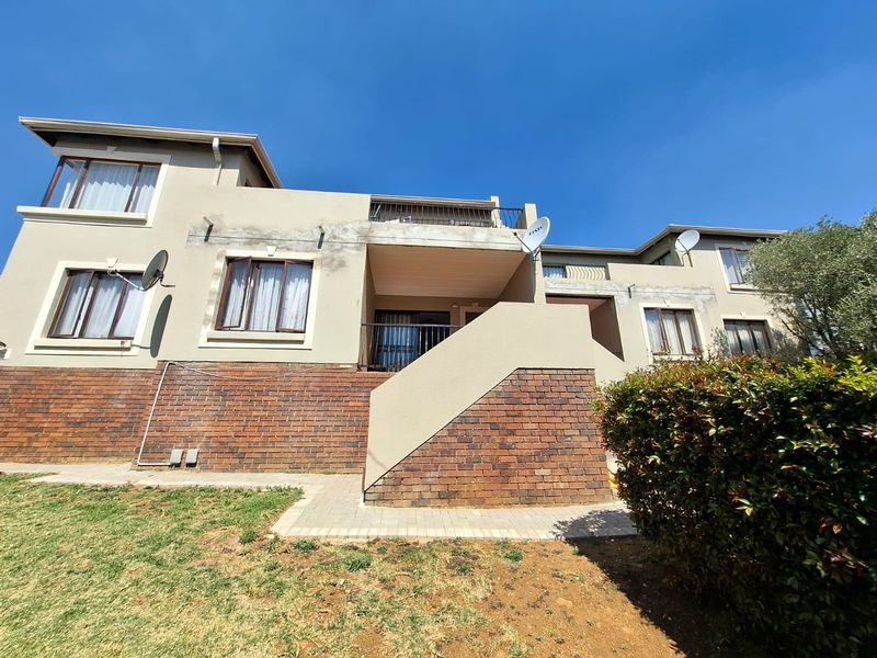Rear view of a multi-story apartment building featuring brick and plaster facade, balconies with metal railings, and a paved ground-level walkway.