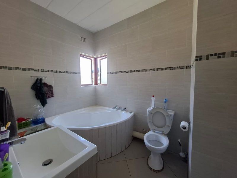 A functional bathroom featuring a corner bathtub, a vanity basin, and a toilet, finished with neutral wall and floor tiling.