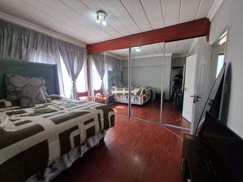 A bedroom featuring laminate flooring and large mirrored built-in cupboards, providing ample storage and reflecting natural light from the window.