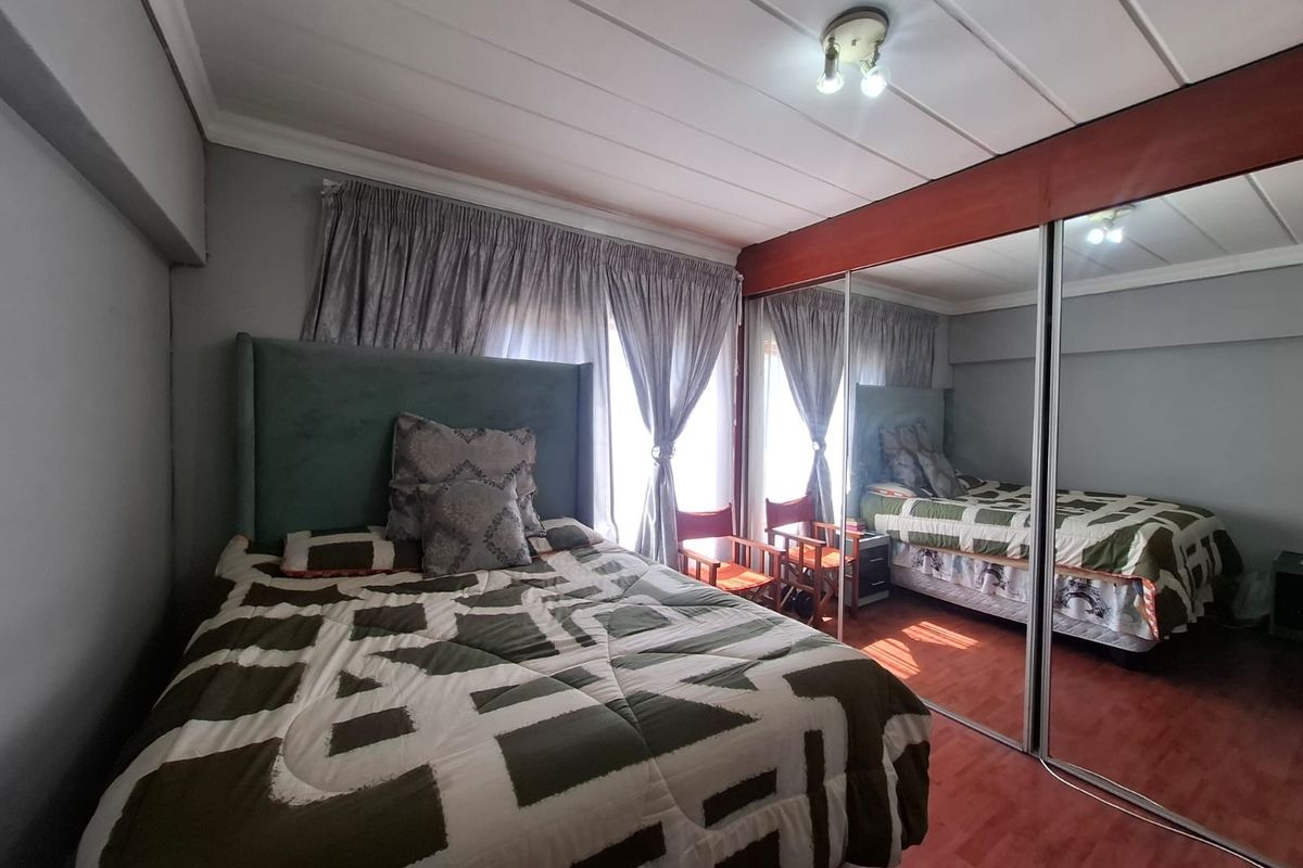 A bedroom featuring laminate flooring and a large built-in mirrored wardrobe, providing ample storage and reflecting natural light from the window.