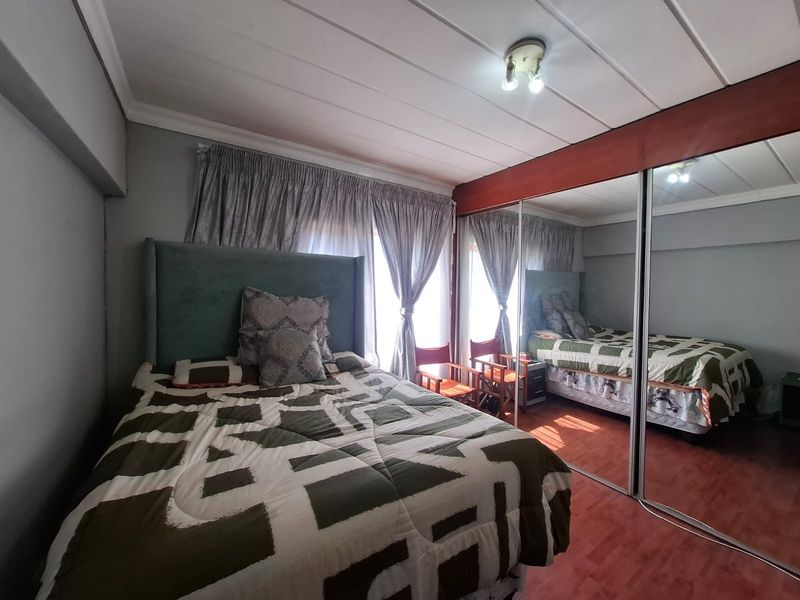 A bedroom featuring laminate flooring and a large built-in mirrored wardrobe, providing ample storage and reflecting natural light from the window.
