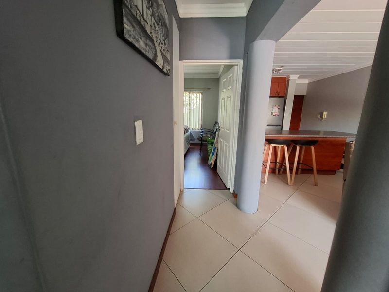 Open plan living area featuring tiled flooring, a structural column, and a kitchen with a breakfast counter, leading into a bedroom.