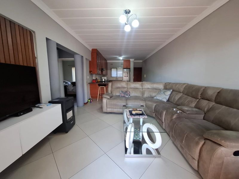 Open-plan living area featuring tiled flooring and wooden ceiling panels, flowing into a functional kitchen space with built-in cabinetry.