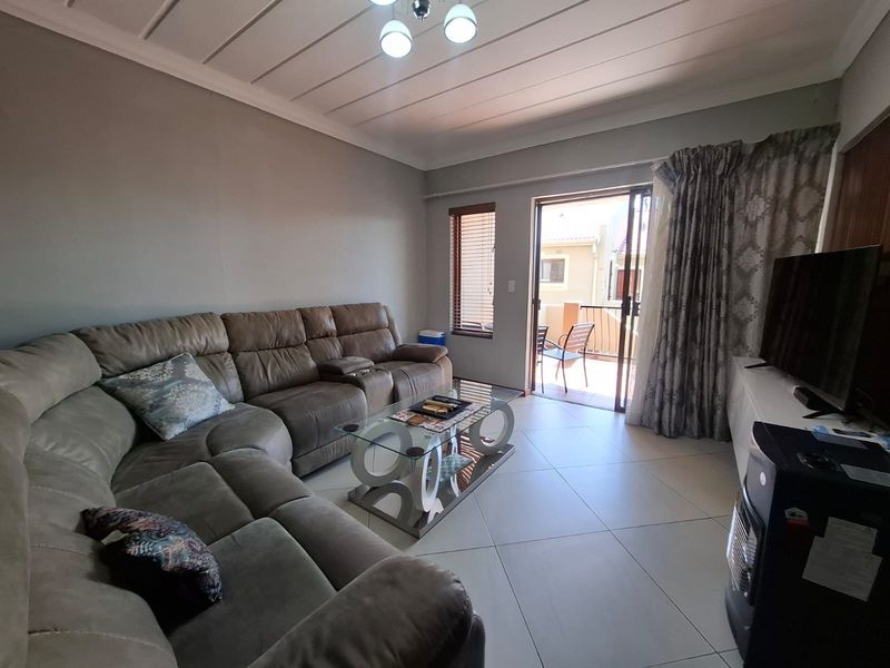 A comfortable living room featuring tiled flooring, a panelled ceiling, and a sliding glass door providing access to an outdoor balcony area.