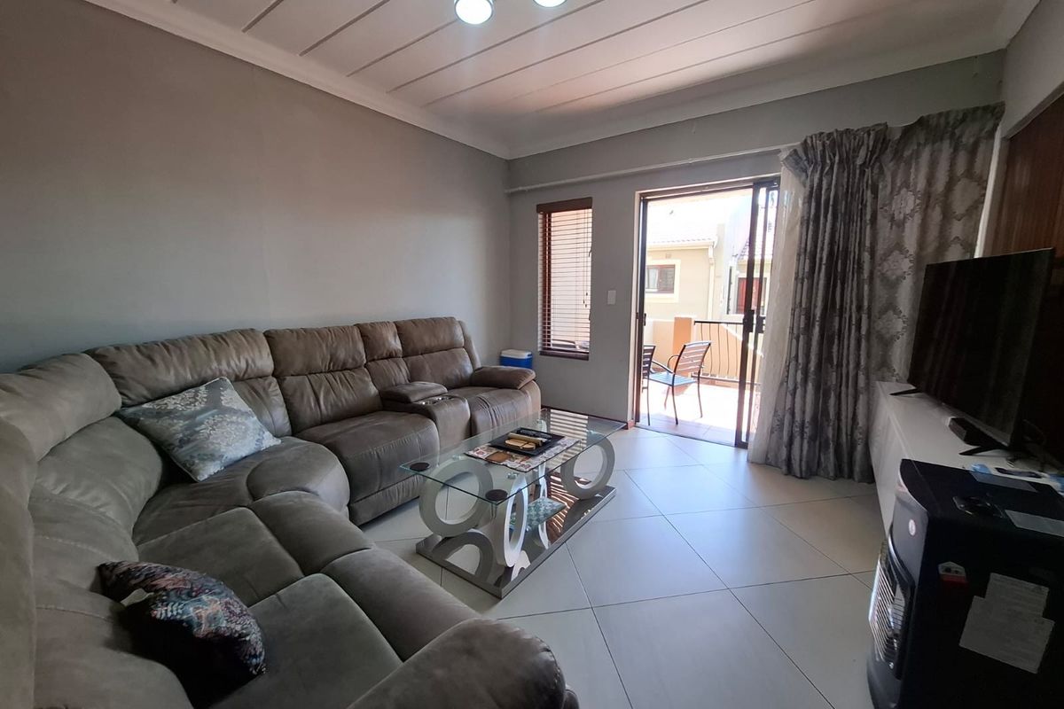 A comfortable living room featuring tiled flooring, a panelled ceiling, and a sliding glass door providing access to an outdoor balcony area.
