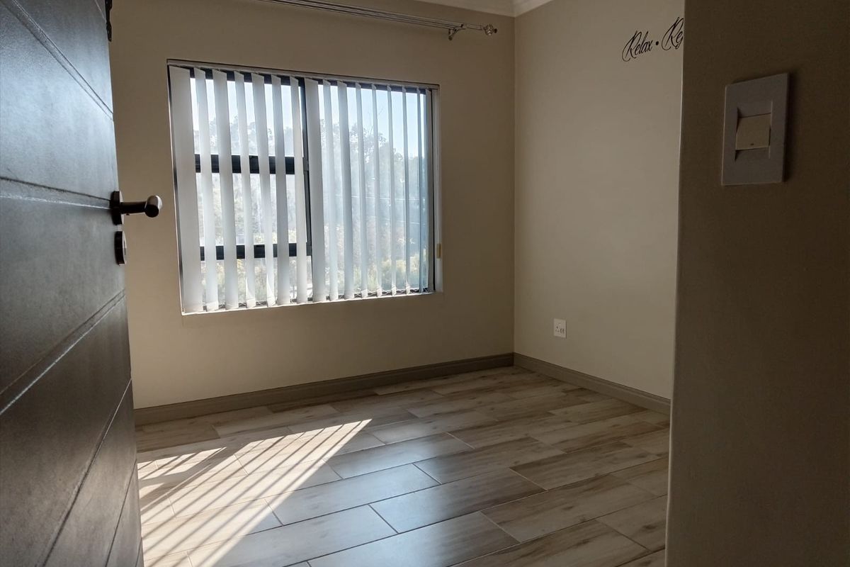 A bright, empty bedroom featuring modern wood-look tile flooring, neutral walls, and vertical window blinds, offering a clean and versatile living space.