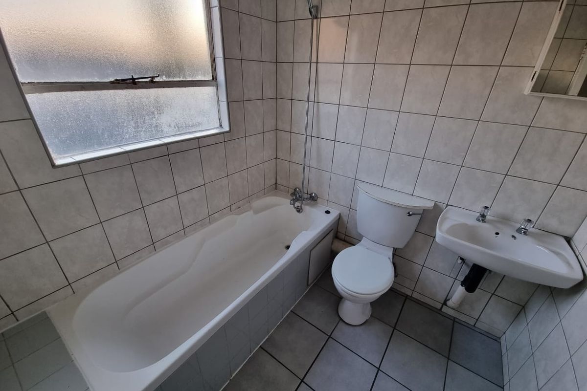 A functional bathroom featuring a bathtub with shower mixer, toilet, and wall-mounted basin, finished with neutral wall and floor tiling.