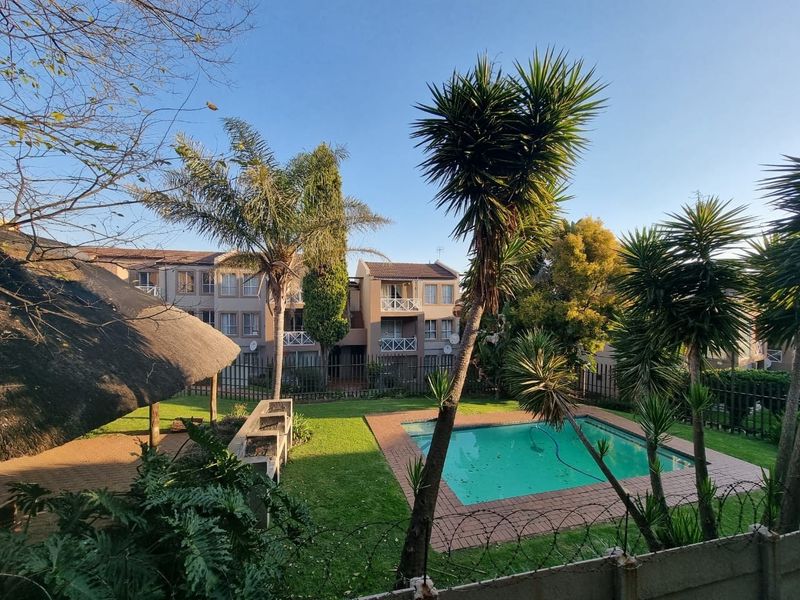 Communal outdoor area featuring a swimming pool, thatched lapa, and built-in braai facilities set within a well-maintained garden.