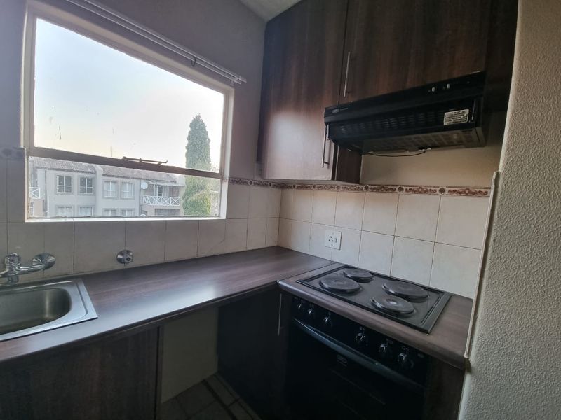 Compact kitchen featuring dark wood-look cabinetry, laminate countertops, built-in oven, electric hob, and a tiled backsplash with a window view.