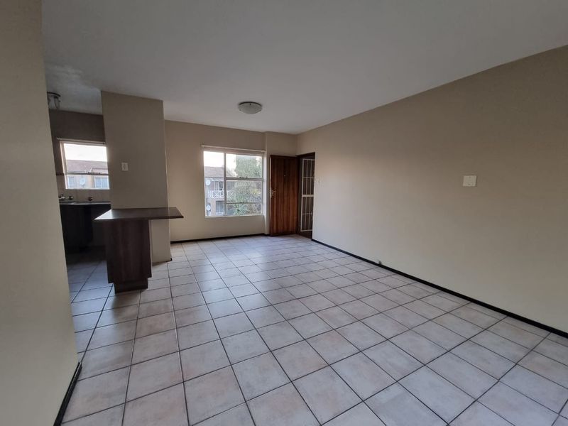 An open-plan living and kitchen area featuring neutral tiled flooring, a breakfast bar, and natural light from large windows.