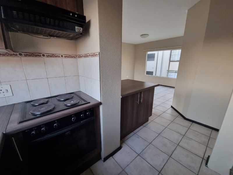 A functional kitchen area featuring built-in cabinetry, an electric hob, oven, and extractor fan, with tiled flooring and a neutral color palette.
