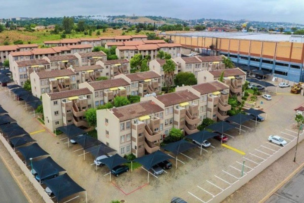 Aerial view of a townhouse complex featuring multiple residential blocks, dedicated carport parking bays, and paved access roads within a secure estate.