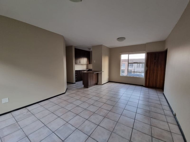 An open-plan living and kitchen area featuring tiled flooring, dark wood cabinetry, a breakfast counter, and natural light from a large window.