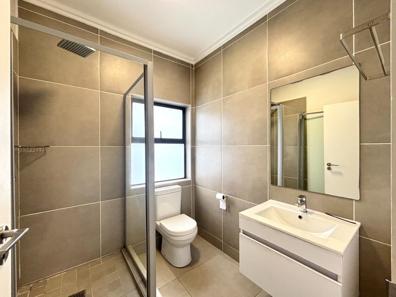 Modern bathroom featuring large format wall tiles, a walk-in shower with a rain shower head, and a sleek wall-mounted vanity unit.