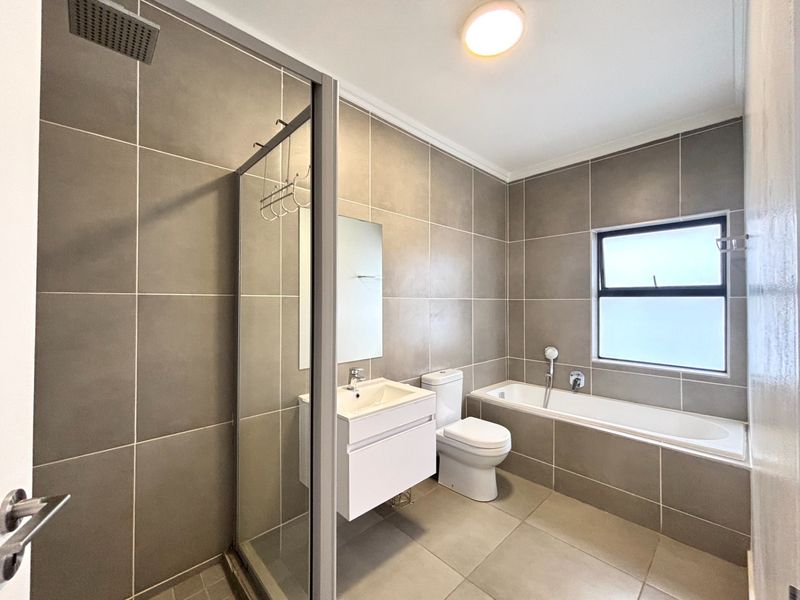 Modern bathroom featuring a walk-in shower with glass enclosure, a separate bathtub, a vanity unit with basin, and neutral floor-to-ceiling wall tiles.