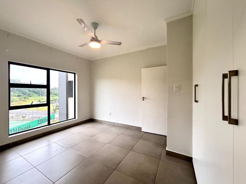 A bright, empty bedroom featuring neutral tiled flooring, built-in cupboards, and a ceiling fan, offering a clean and versatile space.