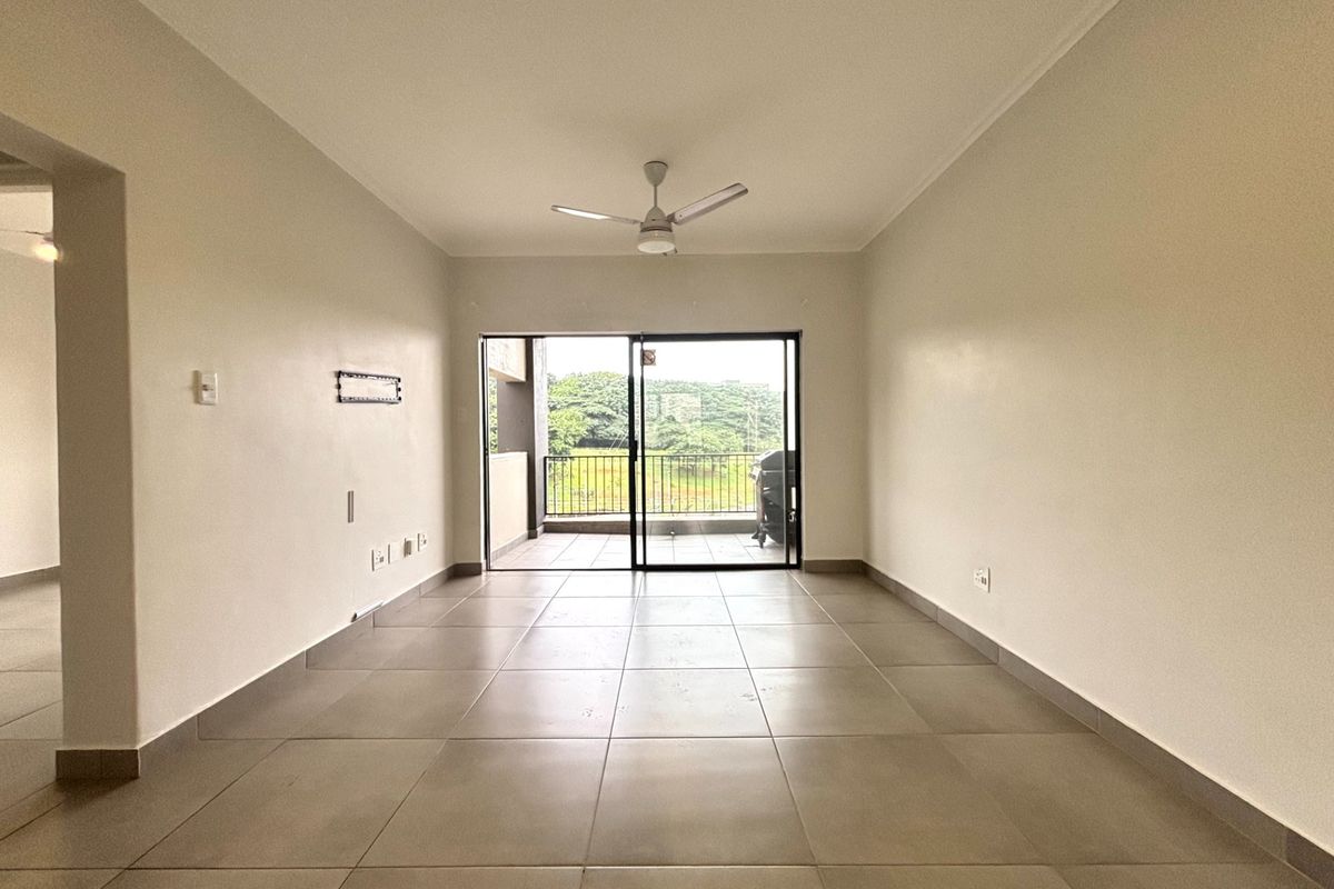 An empty, well-lit living room featuring neutral tiled flooring, a ceiling fan, and sliding glass doors leading to an outdoor balcony area.