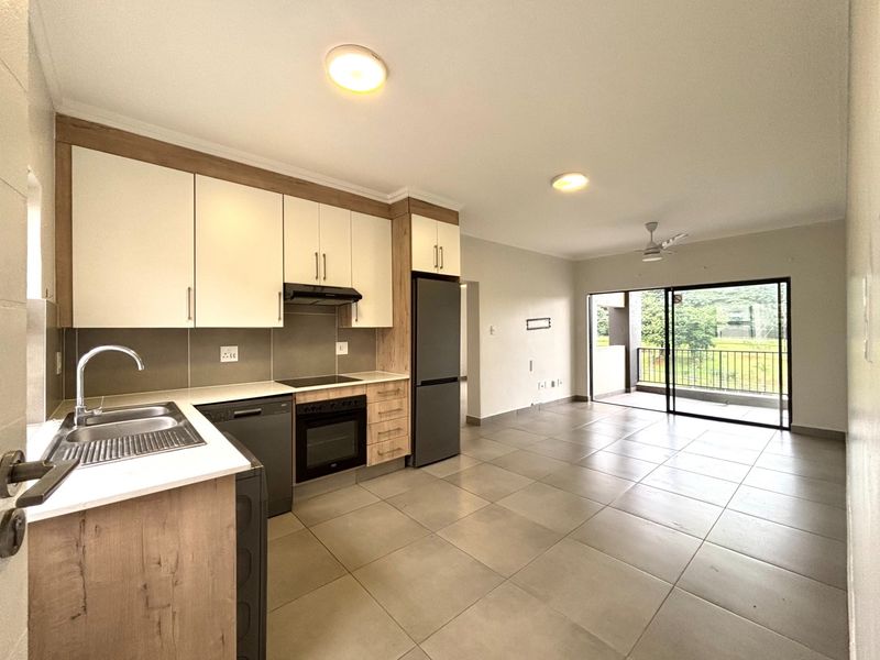 Modern open-plan kitchen and living area featuring sleek cabinetry, integrated appliances, tiled floors, and direct access to a private balcony.