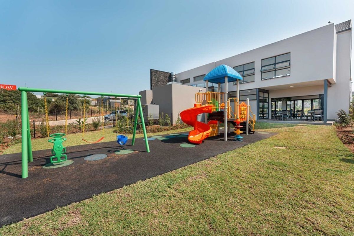 A well-maintained communal outdoor area featuring a modern playground with rubberized flooring, set against the rear facade of a contemporary apartment building.
