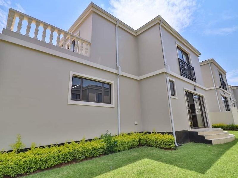 Rear view of a modern two-story house featuring a balcony with a balustrade, sliding glass doors, and a well-maintained garden.