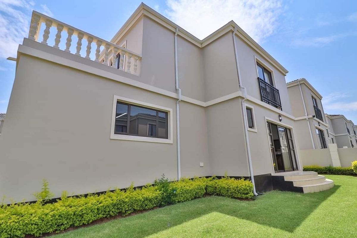 Rear view of a modern two-story house featuring a balcony with a balustrade, sliding glass doors, and a well-maintained garden.