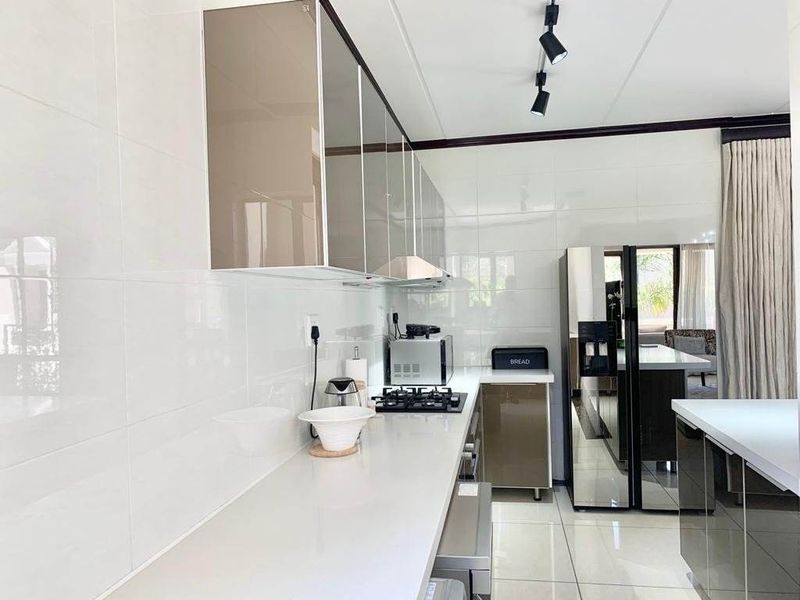 Modern kitchen featuring sleek high-gloss cabinetry, stone countertops, gas hob, extractor fan, and polished floor tiles with contemporary track lighting.