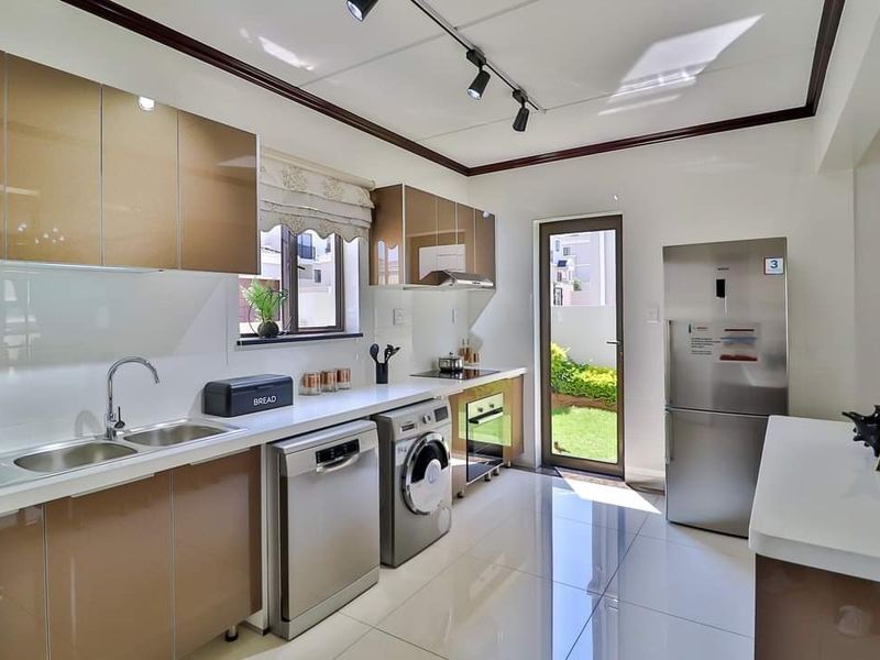 Modern kitchen featuring high-gloss cabinetry, quartz countertops, integrated appliances, and direct access to the rear garden through a glass door.