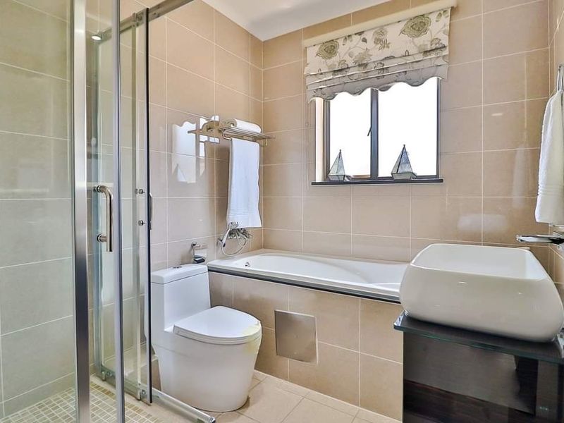 Modern bathroom featuring a glass-enclosed shower, built-in bathtub, vessel sink vanity, and neutral ceramic tiling throughout.