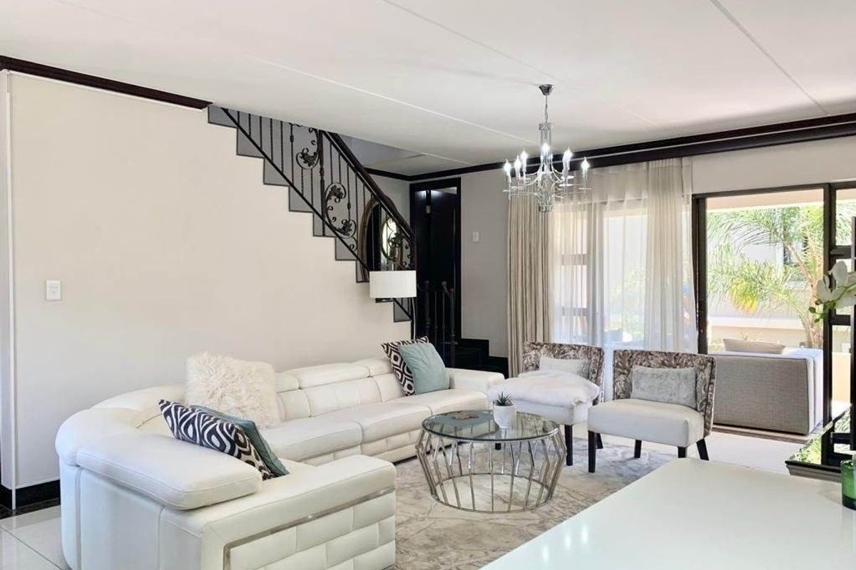 Spacious living room featuring tiled flooring, a decorative wrought iron staircase railing, and large sliding glass doors providing access to the patio.