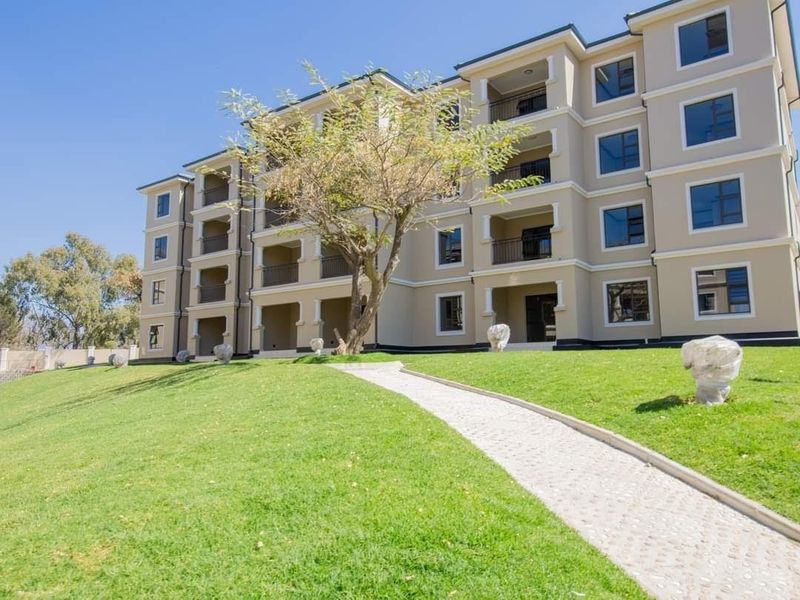 A well-maintained multi-story apartment building featuring private balconies, a paved walkway, and neatly landscaped green lawns.