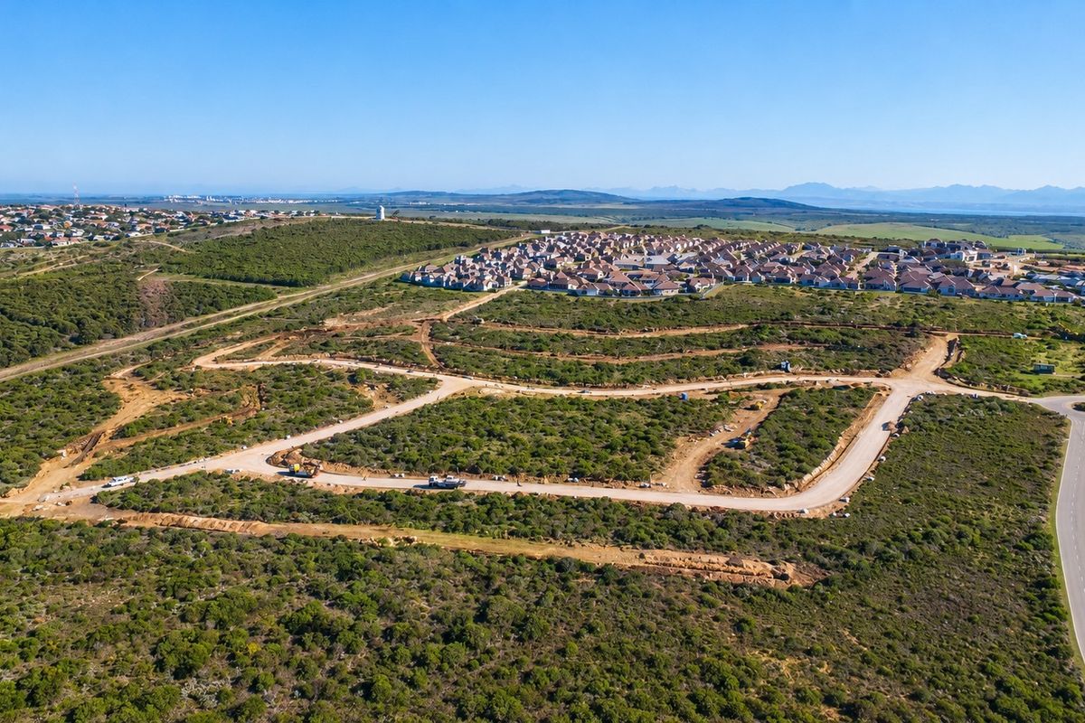 An aerial view of a residential development site featuring cleared plots, paved road infrastructure, and surrounding natural landscape.
