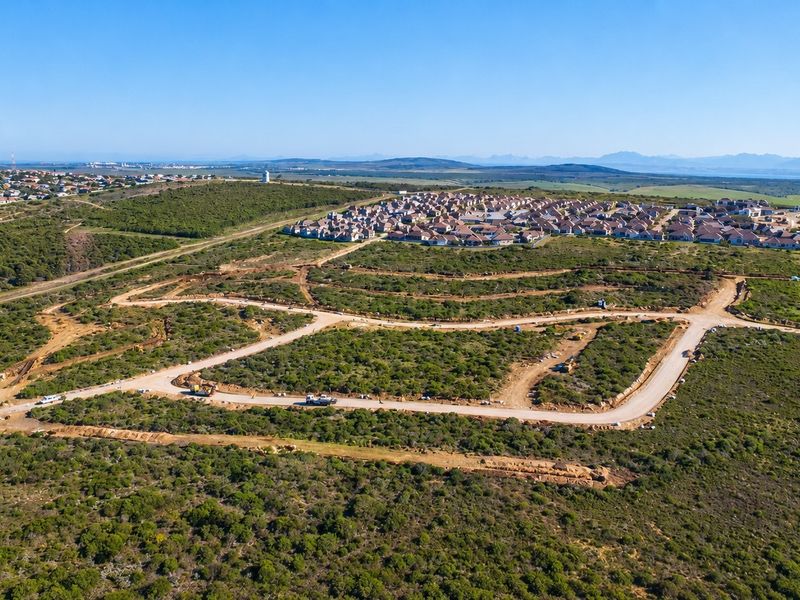 An aerial view of a residential development site featuring cleared plots, paved road infrastructure, and surrounding natural landscape.