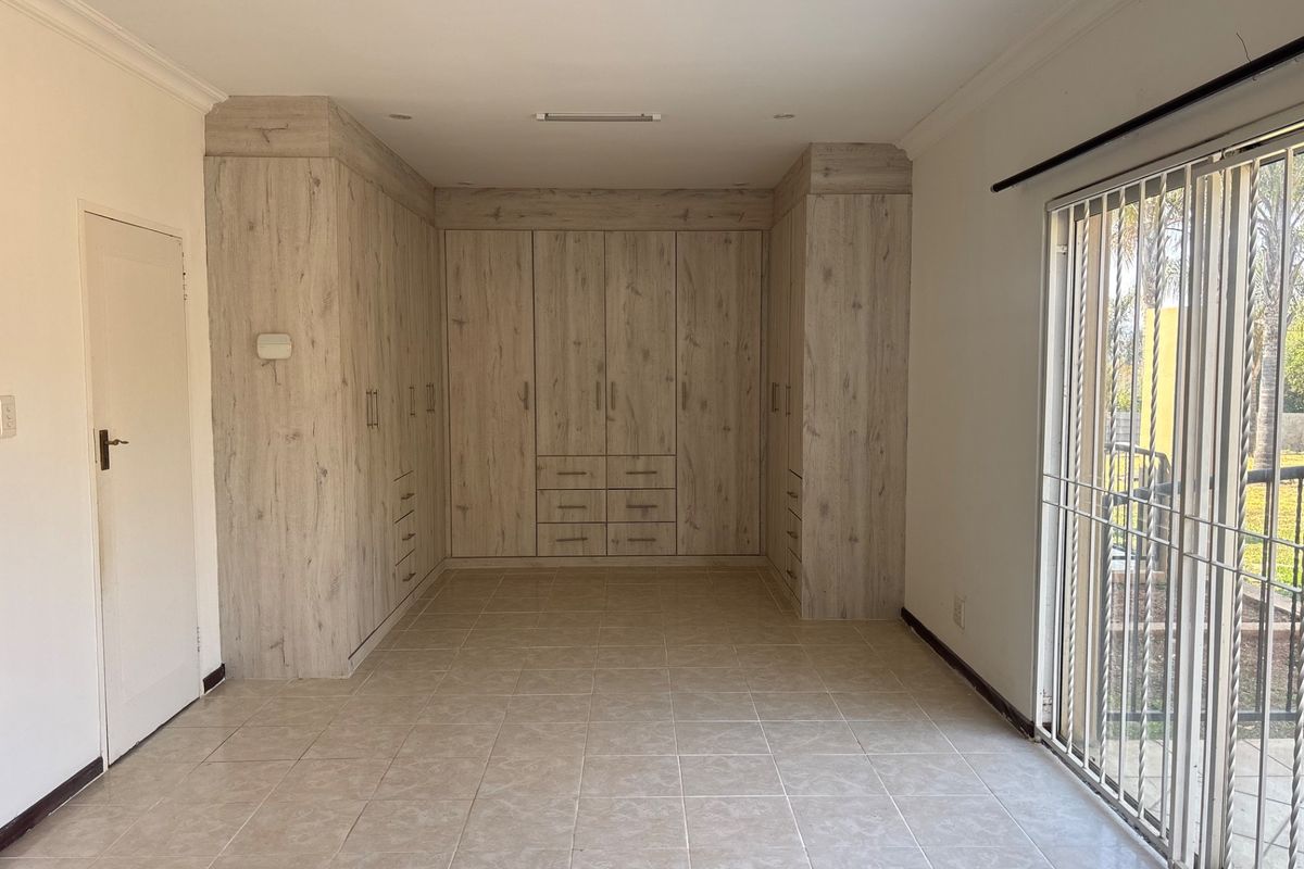 Spacious bedroom featuring extensive built-in wooden cabinetry, neutral tiled flooring, and a sliding glass door providing access to the exterior.