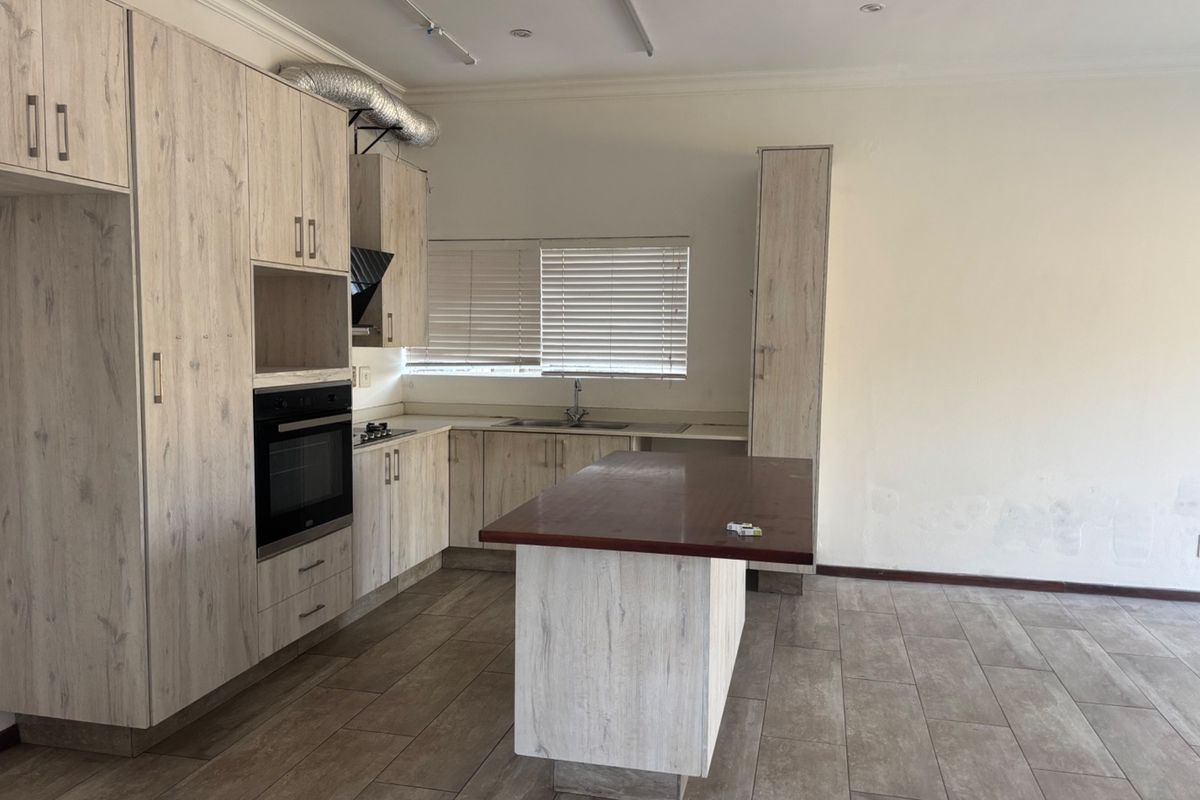 A spacious, empty kitchen featuring light wood-look cabinetry, a central island, built-in oven, and tiled flooring, ready for personalization.