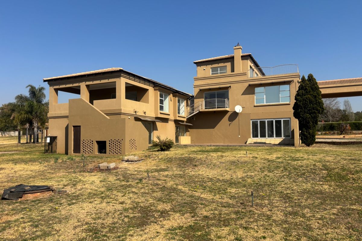 Rear view of a multi-story residential property featuring a balcony, terracotta roof tiles, and a large garden area.