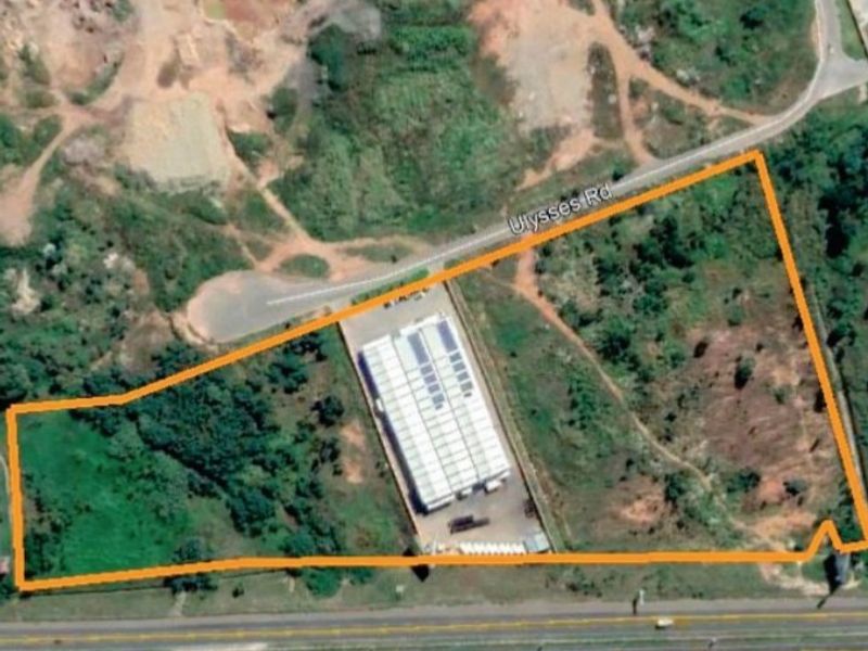 Aerial view of a vacant agricultural land plot featuring an existing industrial warehouse building with solar panels and direct road access.
