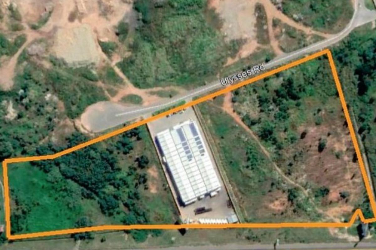 Aerial view of a vacant agricultural land plot featuring an existing industrial warehouse building with solar panels and direct road access.