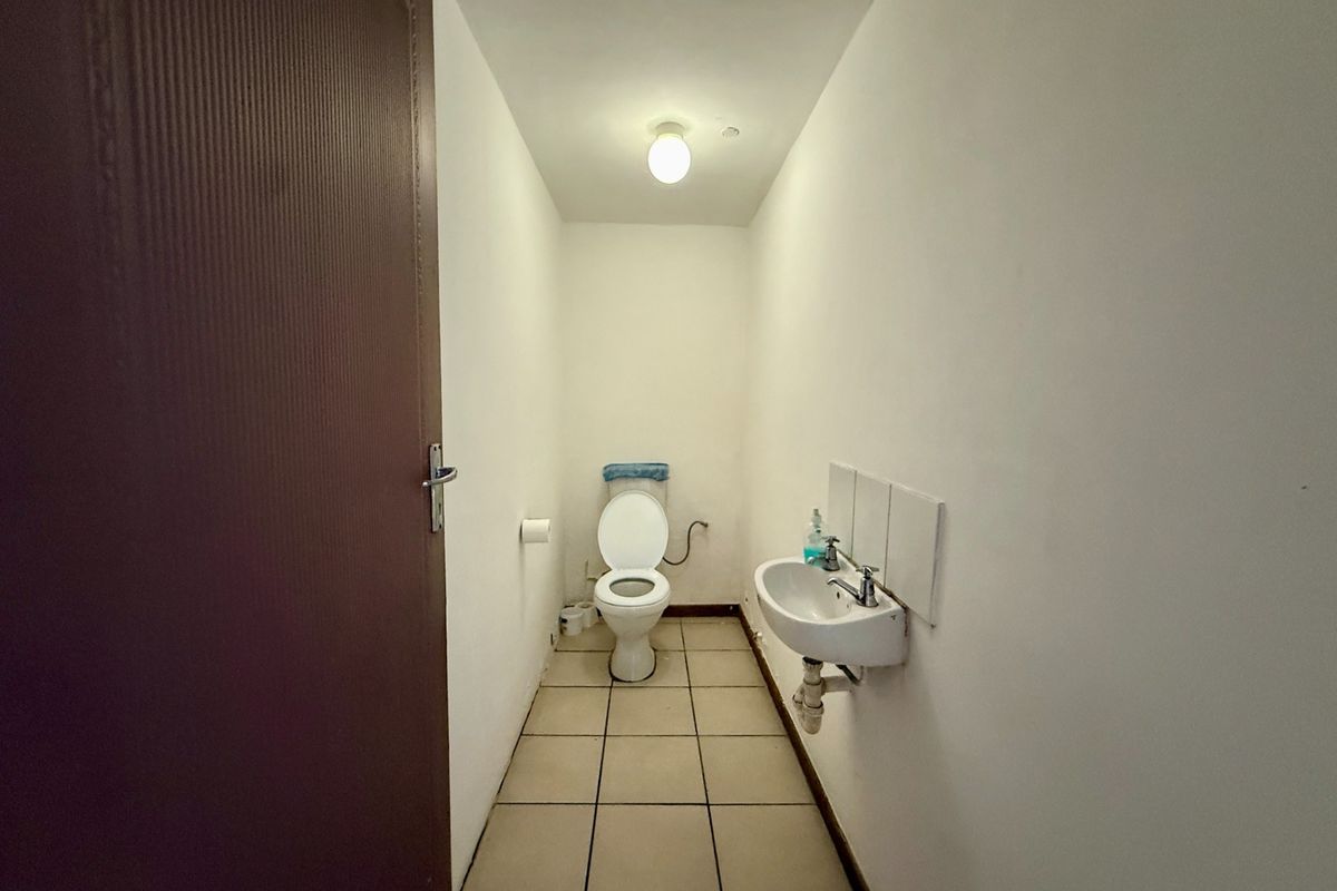 A functional, compact industrial-style restroom featuring a wall-mounted basin, toilet, and tiled flooring with neutral wall finishes.