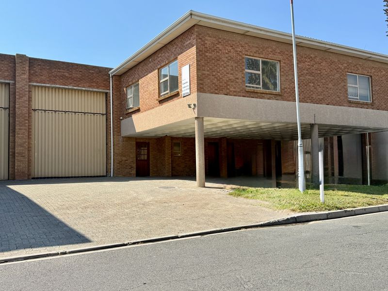 Front exterior view of an industrial property featuring a face brick facade, large roller shutter door, and a covered parking area.