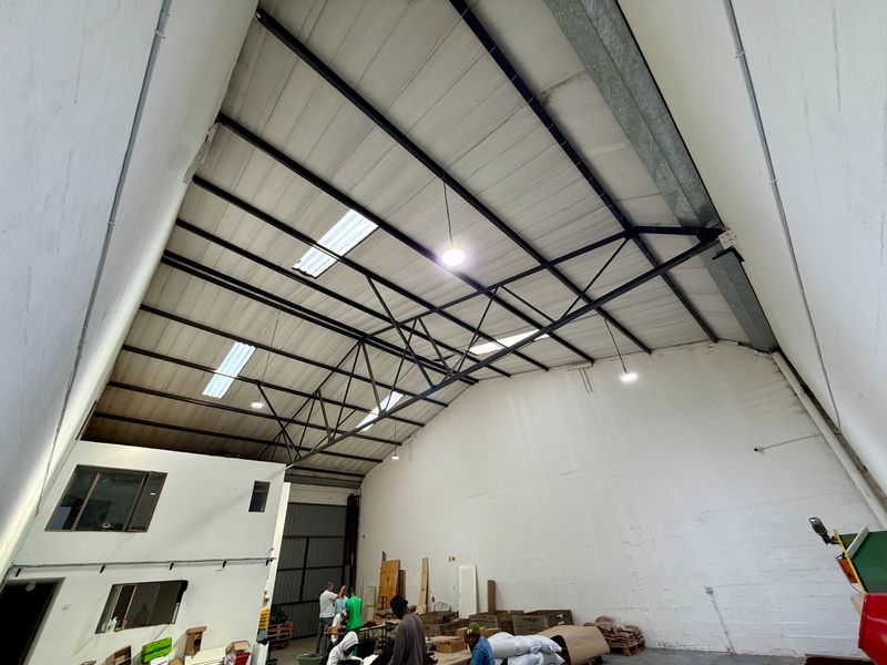 Spacious industrial warehouse area featuring high ceilings with exposed steel trusses, integrated skylights, and a mezzanine level for additional utility or office space.
