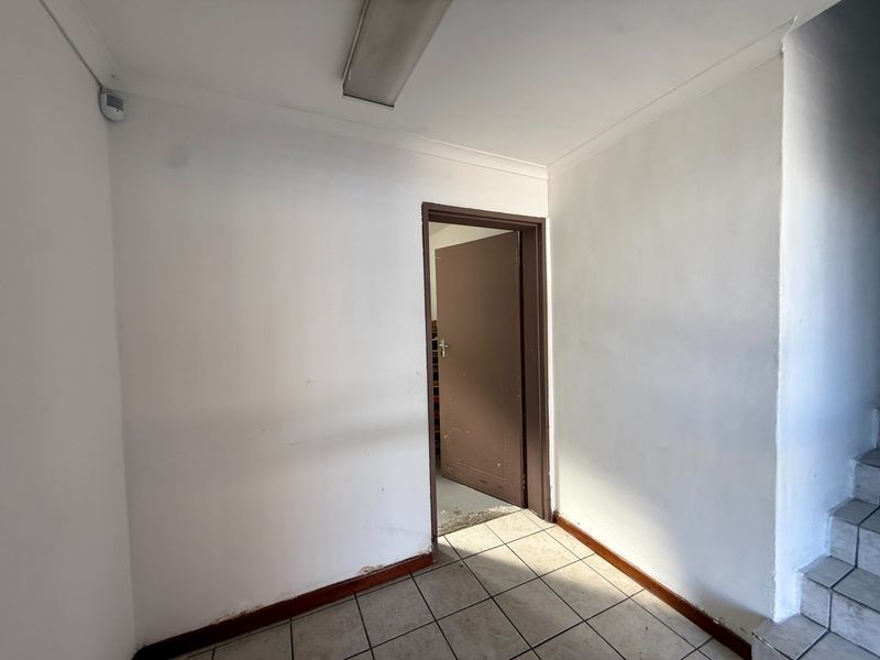 A functional hallway area featuring tiled flooring, a ceiling-mounted light fixture, and a security camera, showing signs of wear and tear.